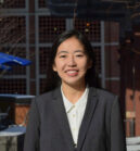 Headshot of a person in formal attire with a background of a building and metal lattice.