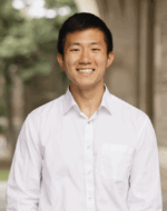 Won-Jae_Chang_photo Headshot of person standing in a white shirt outdoors, with a blurred background of greenery and a stone building.